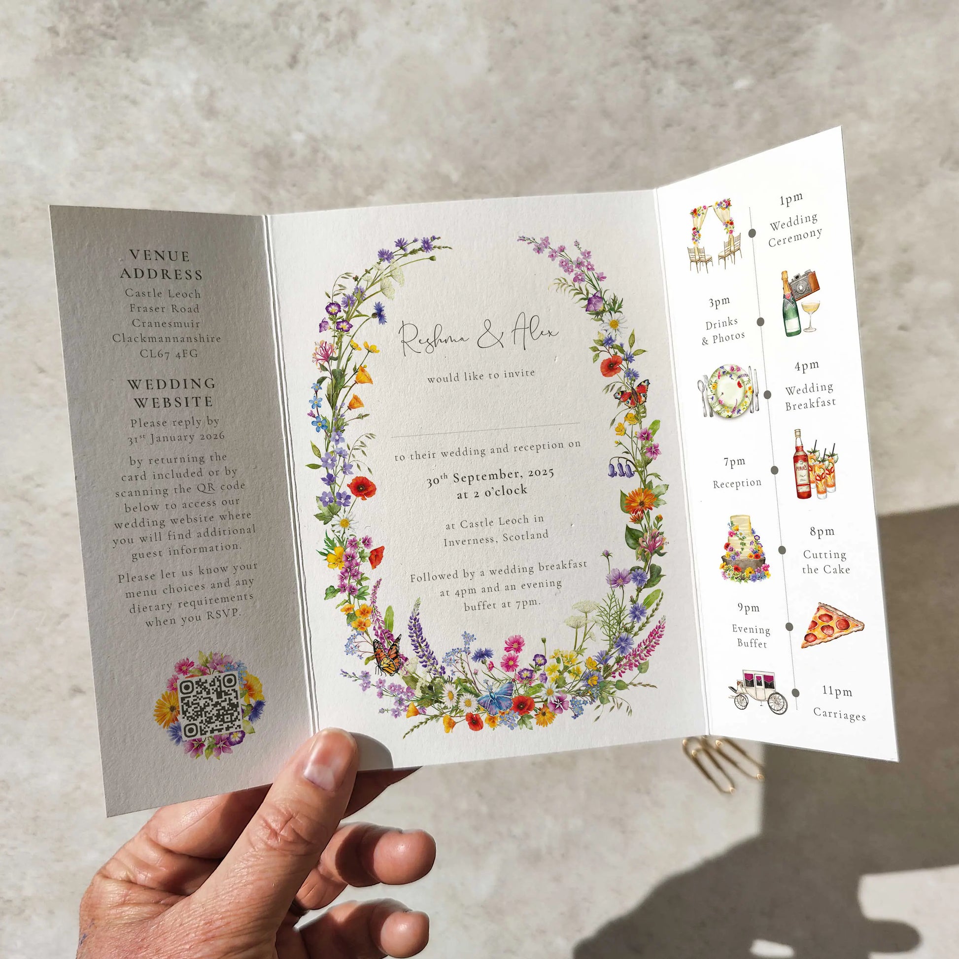 Folded wedding invitation with floral design held by a hand on a neutral background