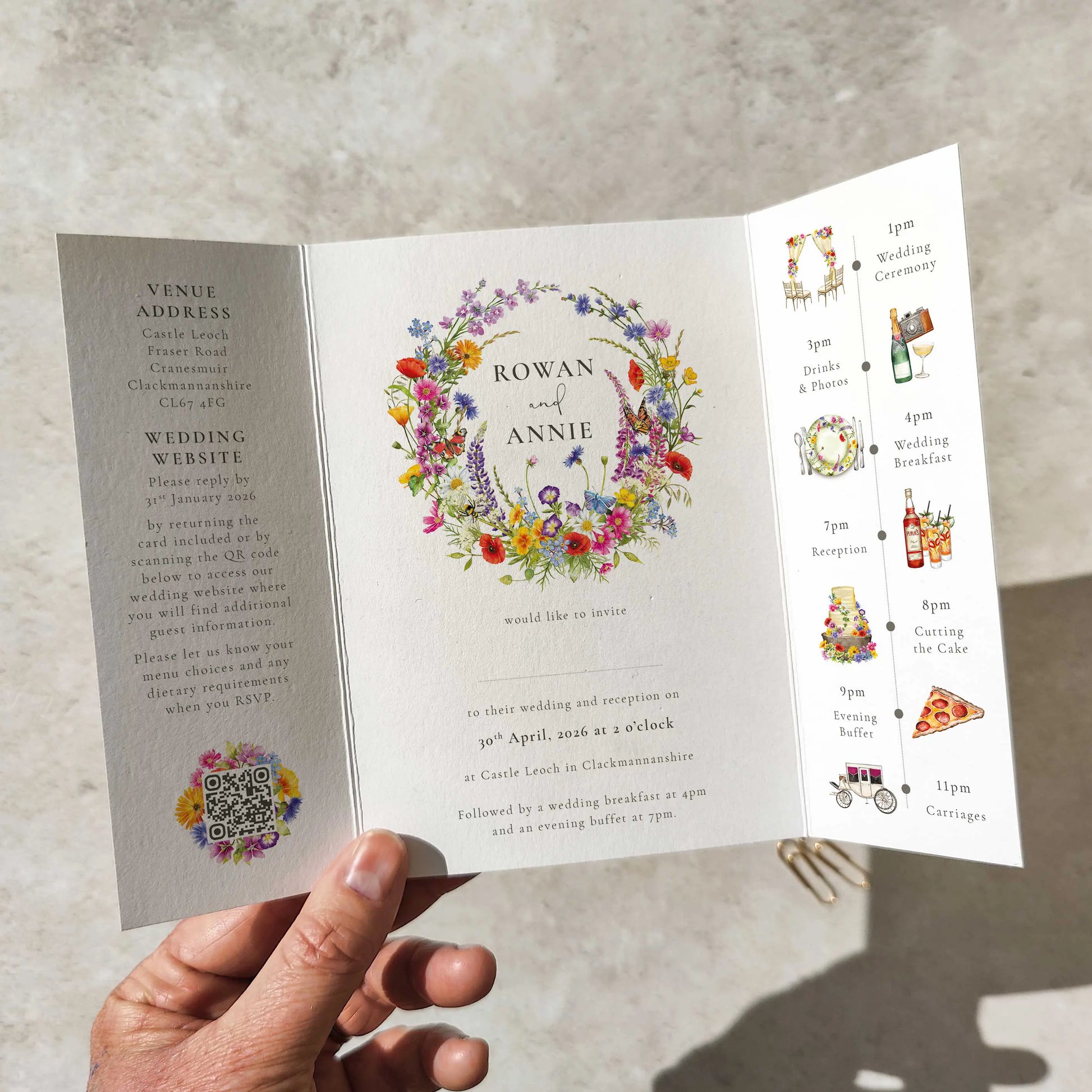 Hand holding a wedding invitation with a colorful floral design and event schedule.