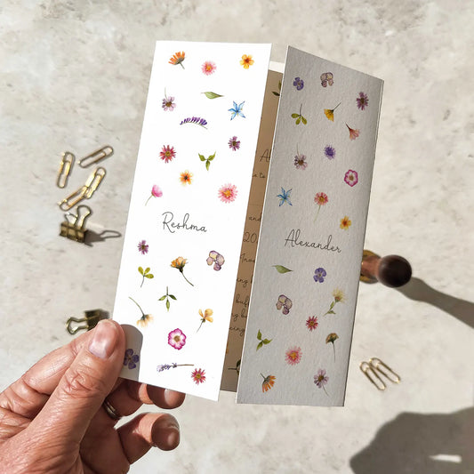 Wedding invitation cards with floral designs held by a hand on a textured surface.