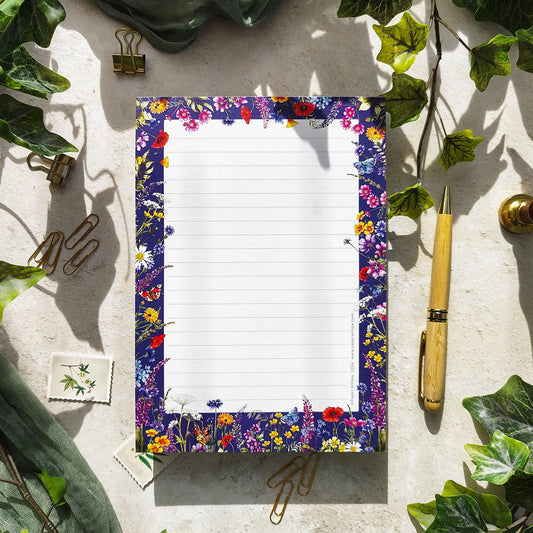 Floral border notepad on a textured surface with greenery and stationery items.