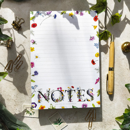 Notepad with floral border and 'NOTES' text on a textured surface with a pen and paper clips.