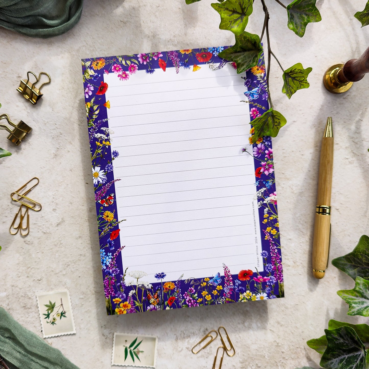A5 size notepad with a floral watercolor design on the cover, labeled 'Wildflower', resting on a table with a pen and decorative items around it.