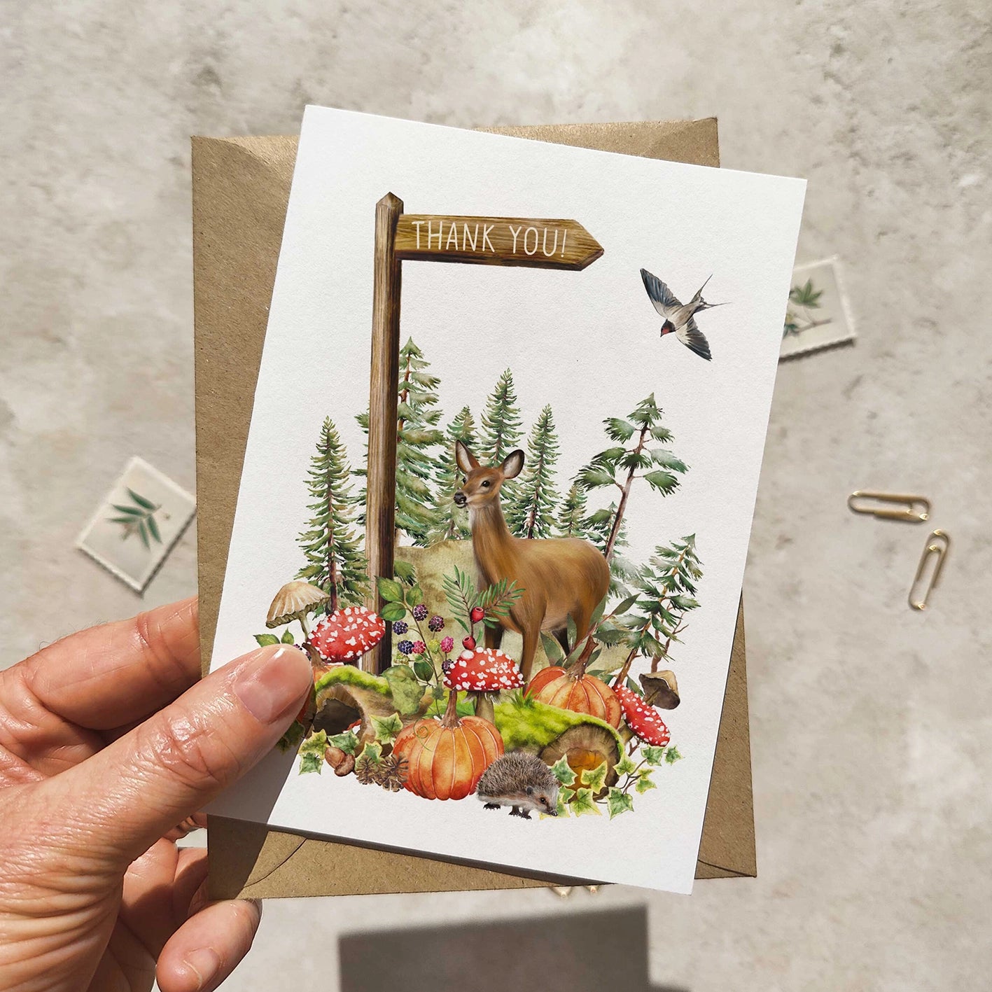 Greeting card with autumn woodland, a deer and nature-themed design held by a hand on a neutral background.