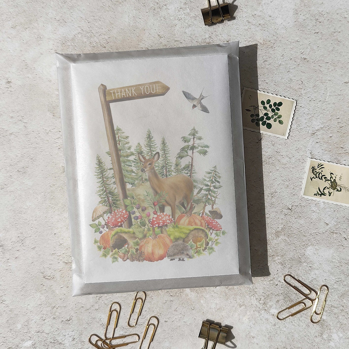 Greeting card with a deer and nature design on a textured surface with paper clips.
