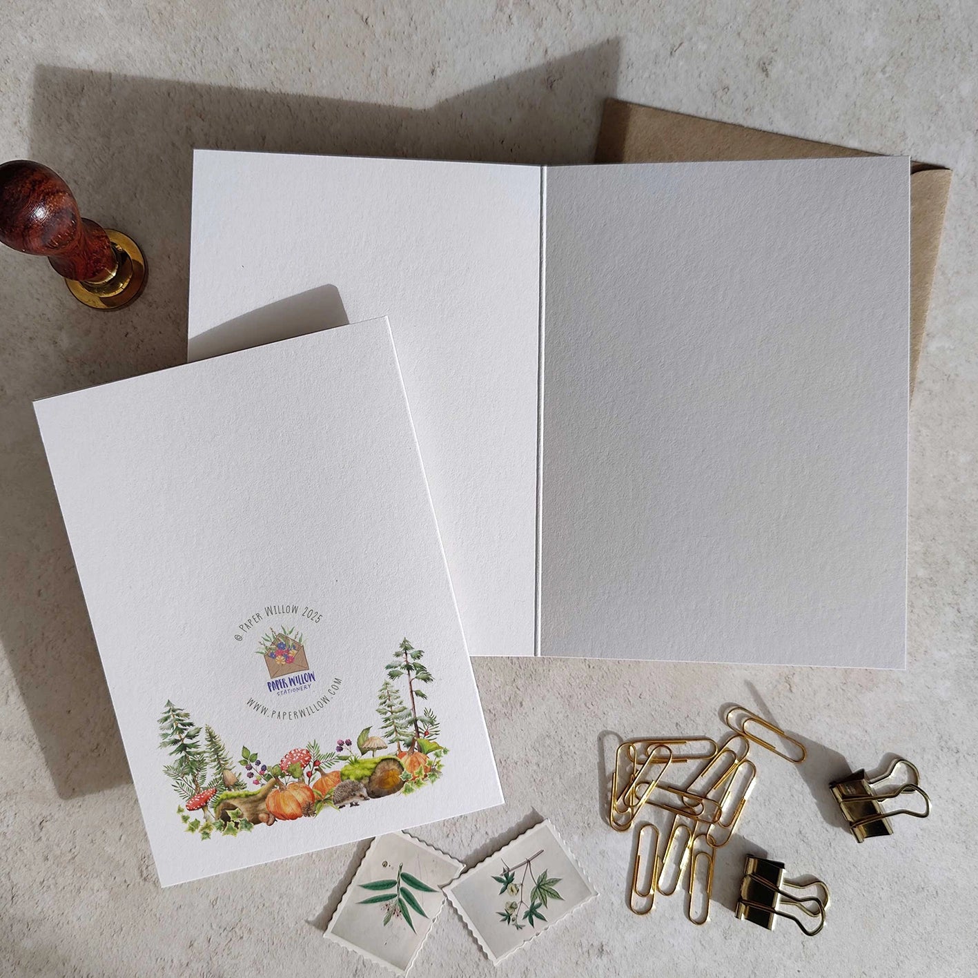 Set of stationery items including a card with a floral design, an envelope, and paper clips on a textured surface.