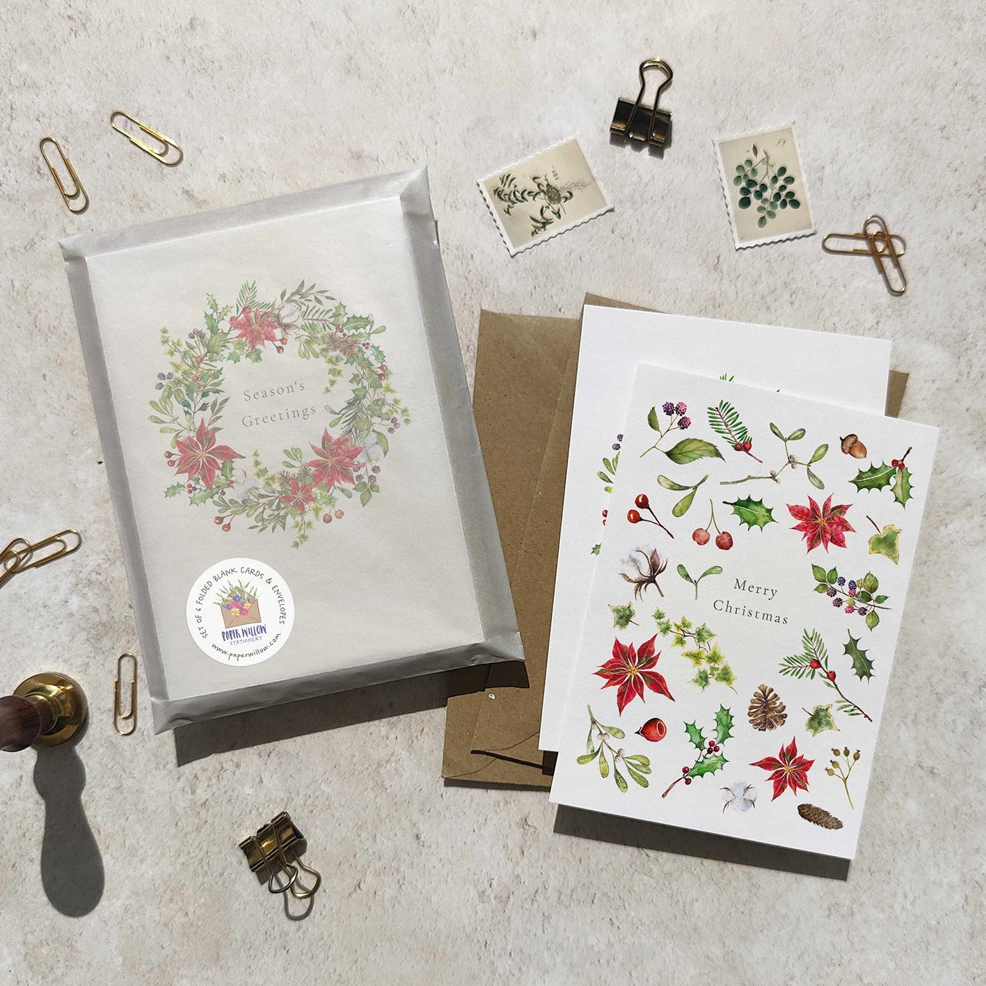 Set of Christmas-themed cards and envelopes on a textured surface with decorative paper clips.