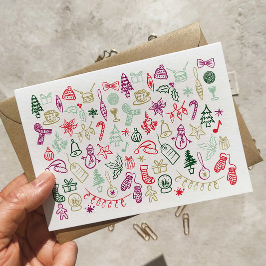 Hand holding a card with Christmas-themed doodles on a concrete surface