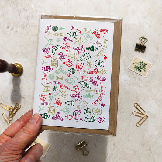 Hand holding a card with Christmas-themed doodles on a textured surface with office supplies.