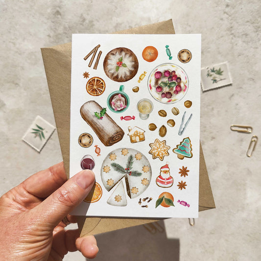 Greeting card with festive food illustrations held by a hand on a textured surface.
