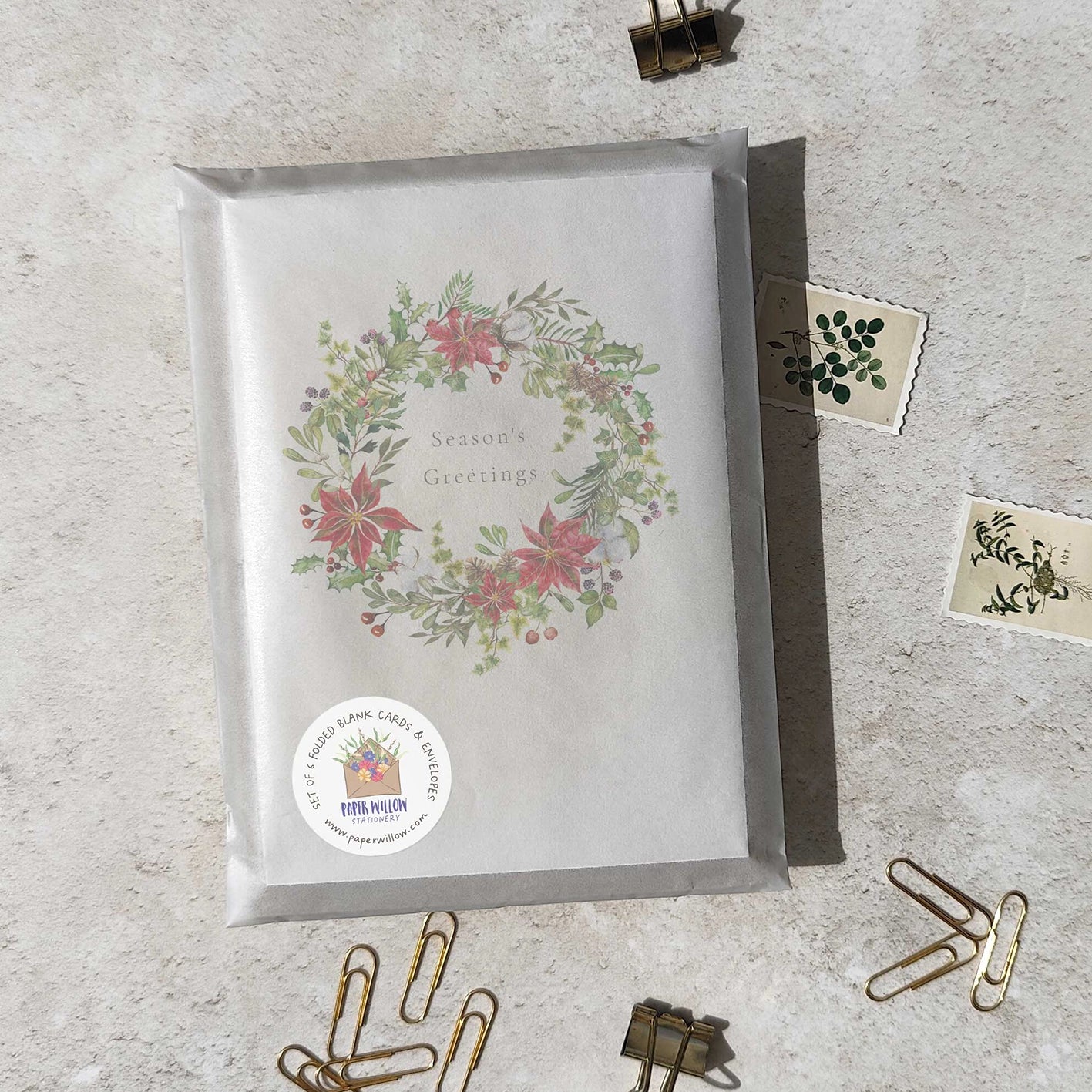 Greeting card with floral wreath design on a textured surface with paper clips.