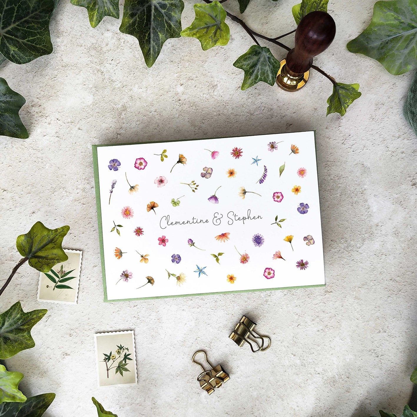 Floral card with personalized names on a textured surface with greenery