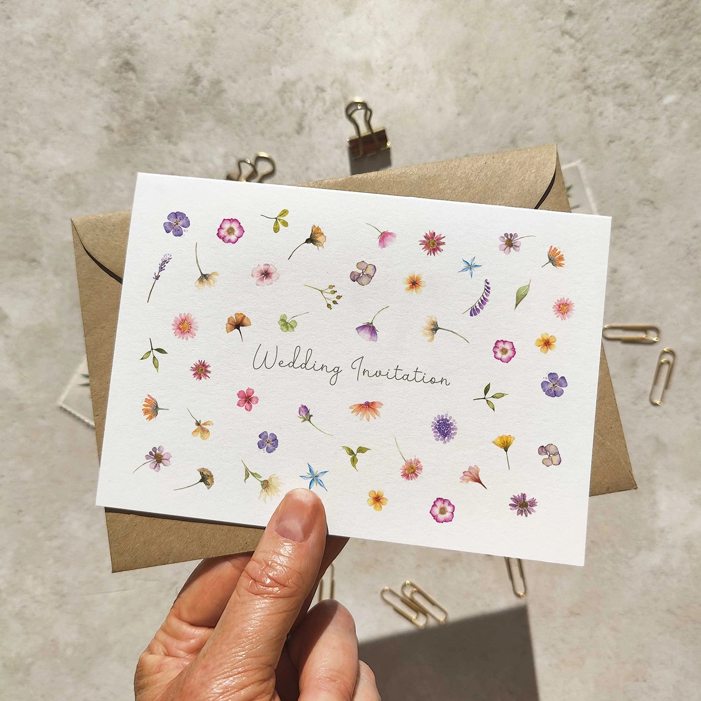 Folded wedding invitation with a wildflower pattern held up with an envelope.