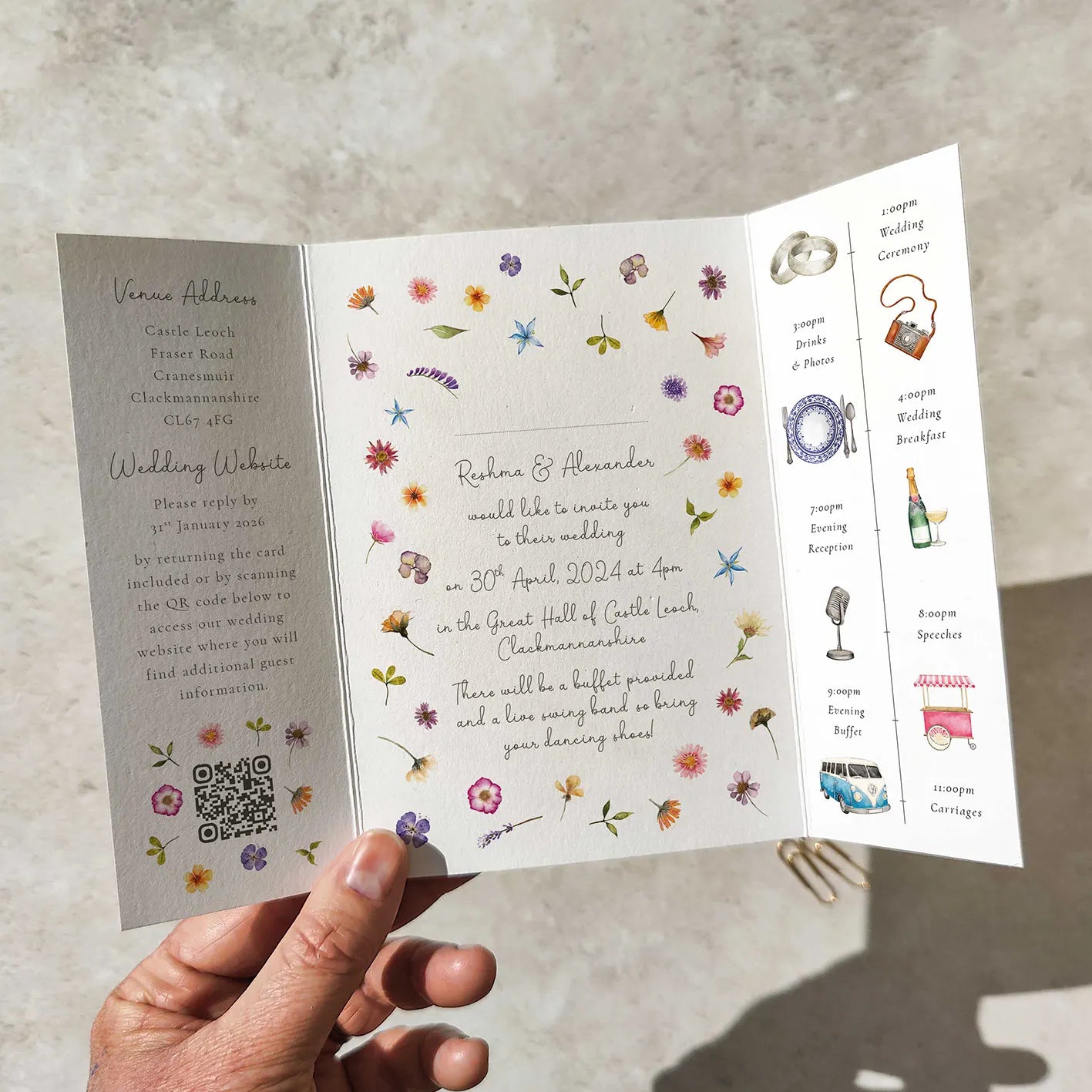 Hand holding a floral wedding invitation with event details.