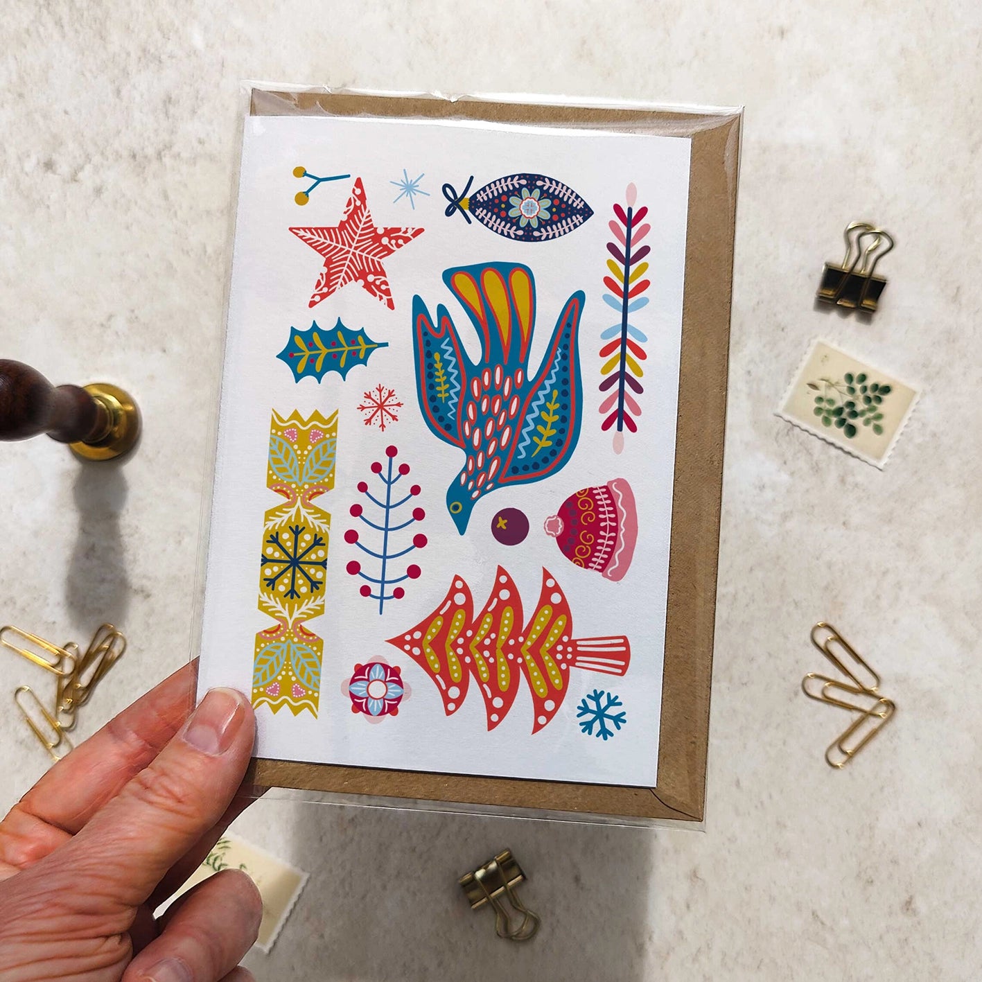 Hand holding a card with colorful illustrations of a bird, fish, and abstract shapes on a textured surface.