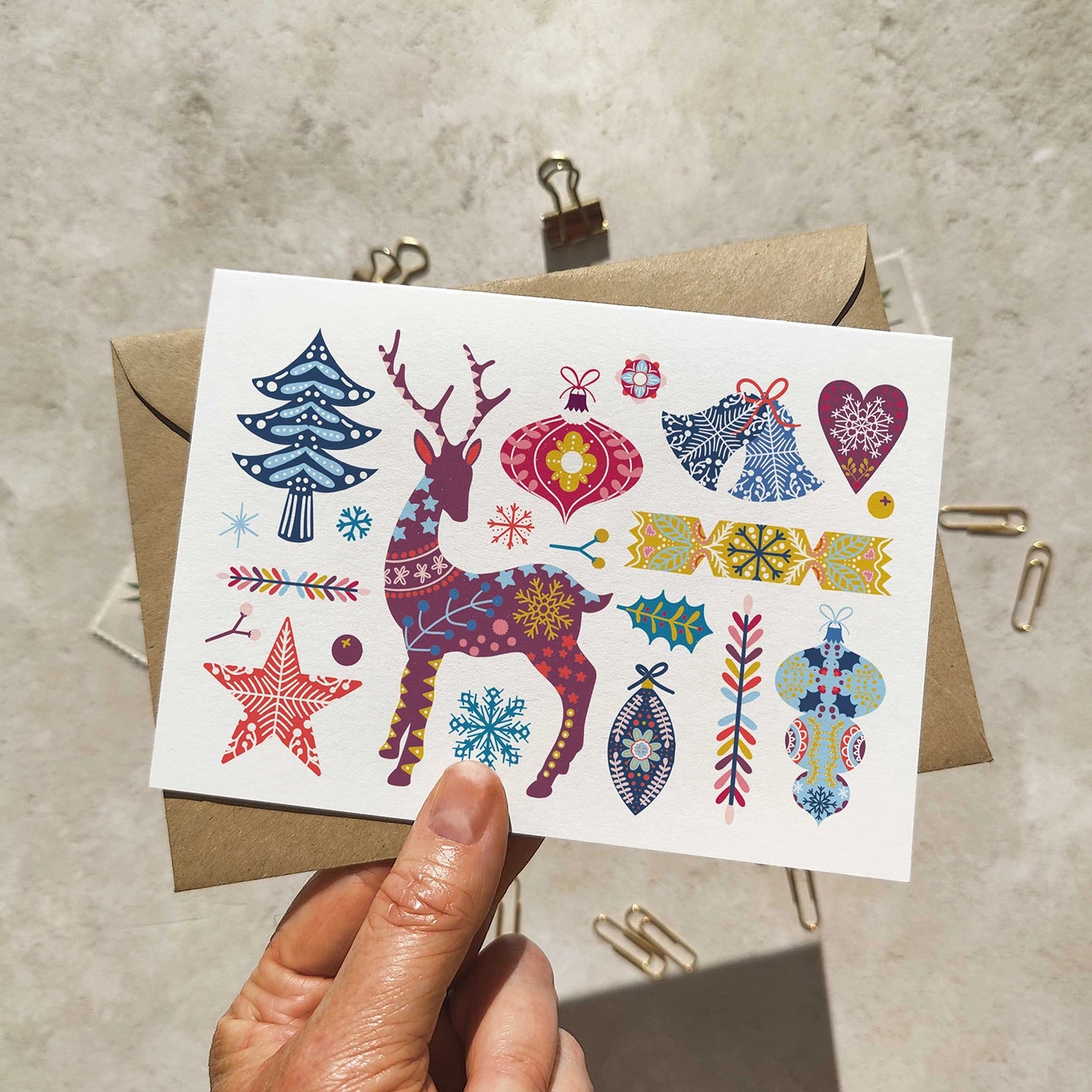 Colorful Christmas-themed tattoos on a white card held by a hand with a brown envelope in the background.
