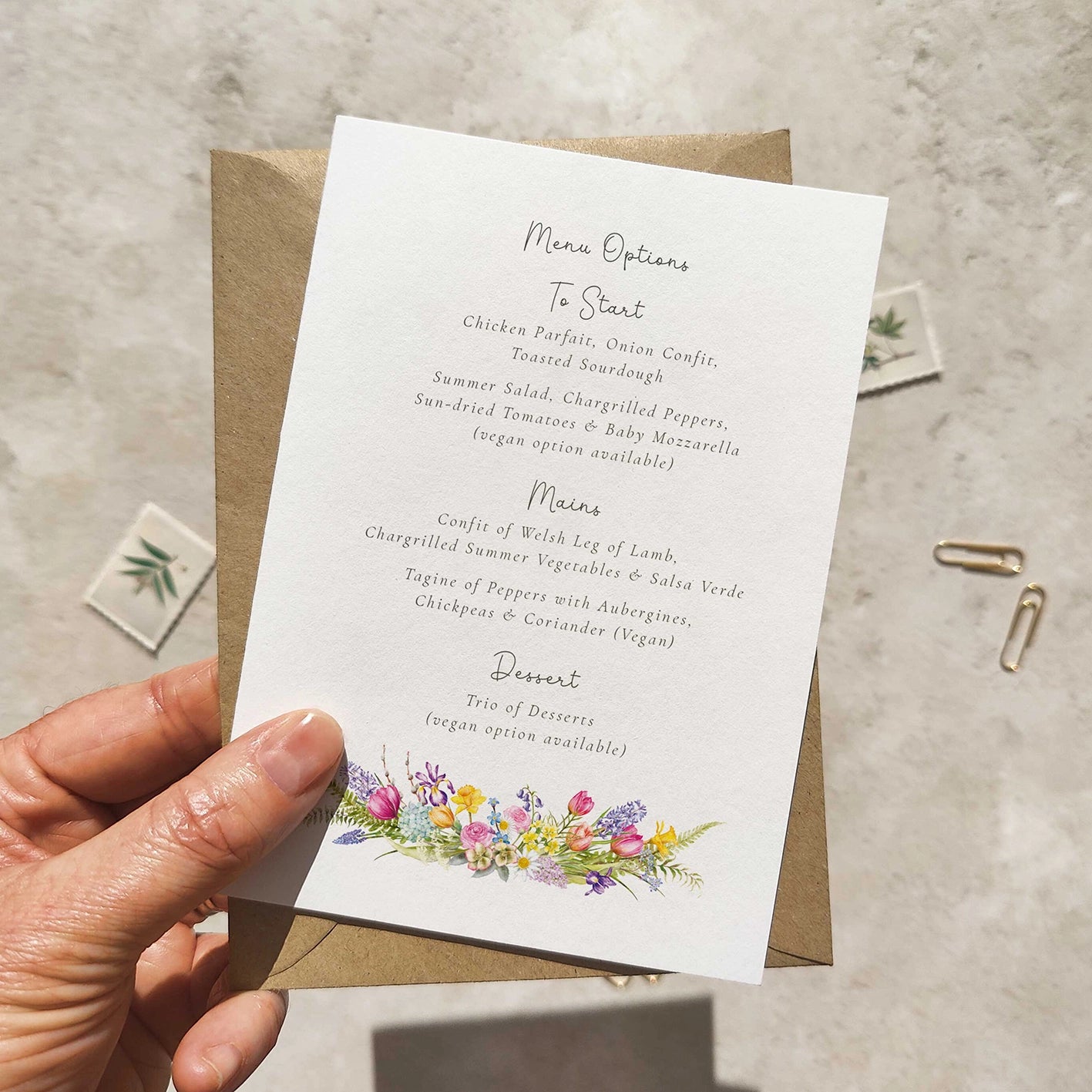 Hand holding a wedding invitation with floral design on a textured surface