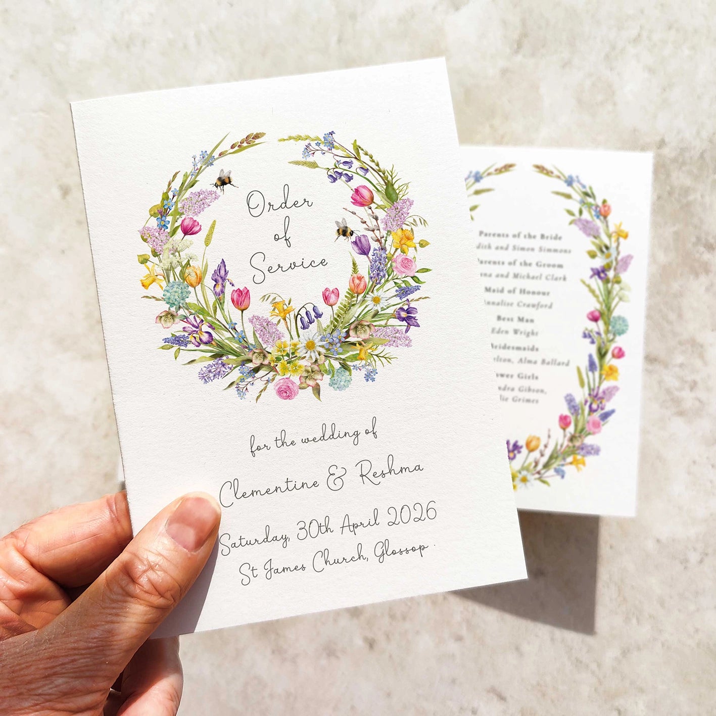 Hand holding a wedding order of service with floral design on a textured surface