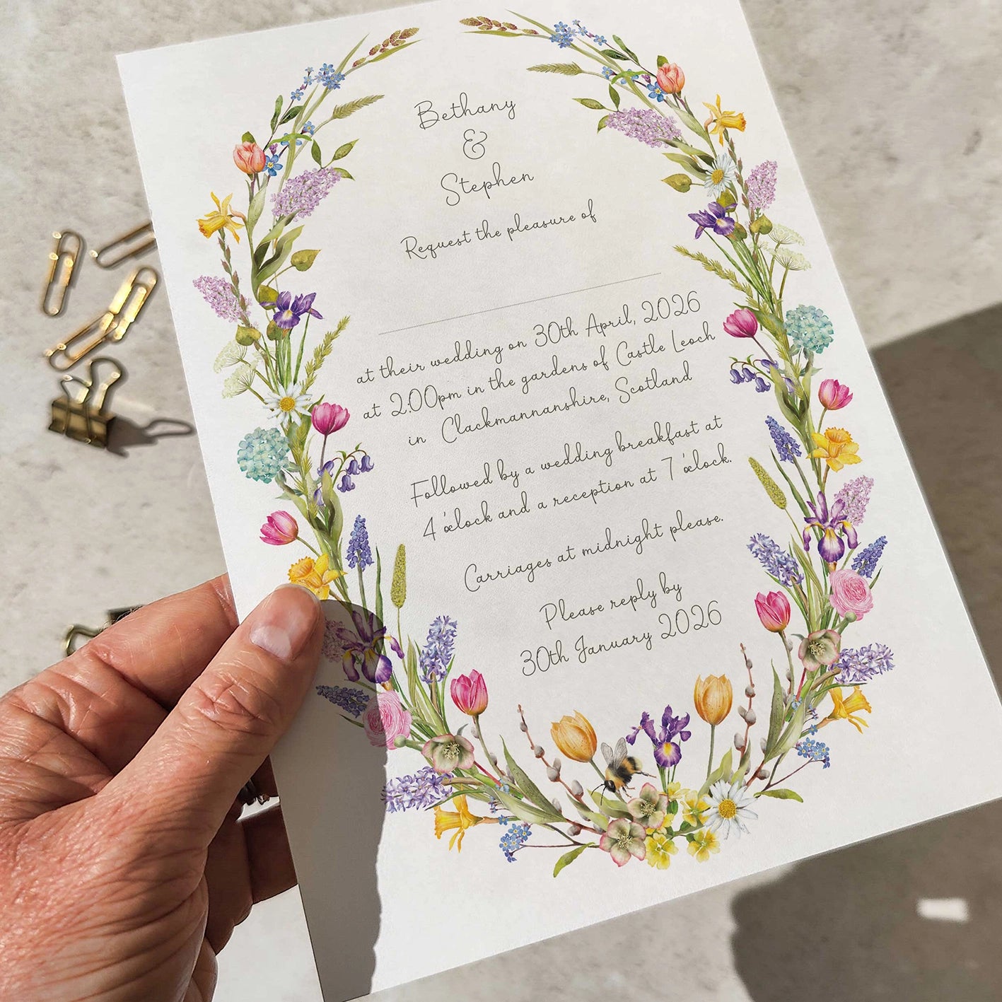 Hand holding a wedding invitation with floral design on a neutral background