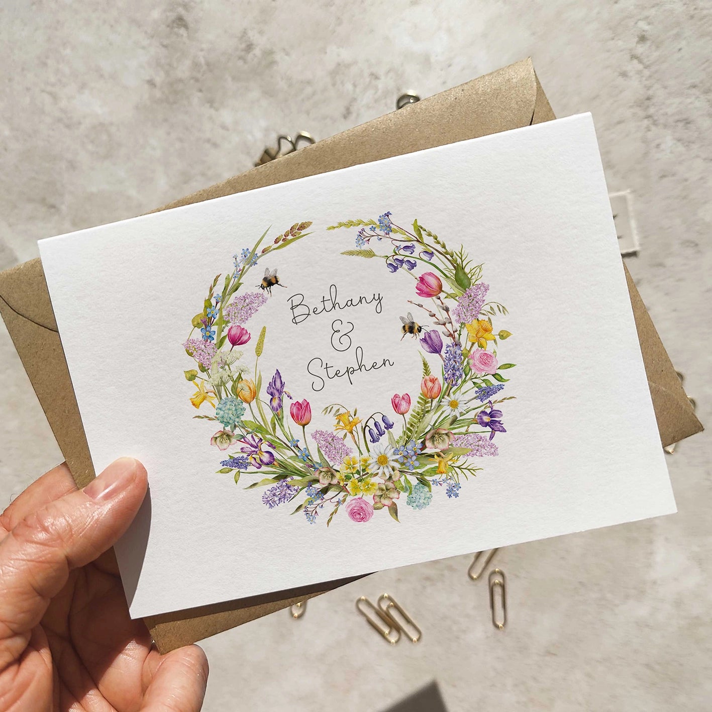 Wedding invitation with floral design and text held by a hand on a neutral background