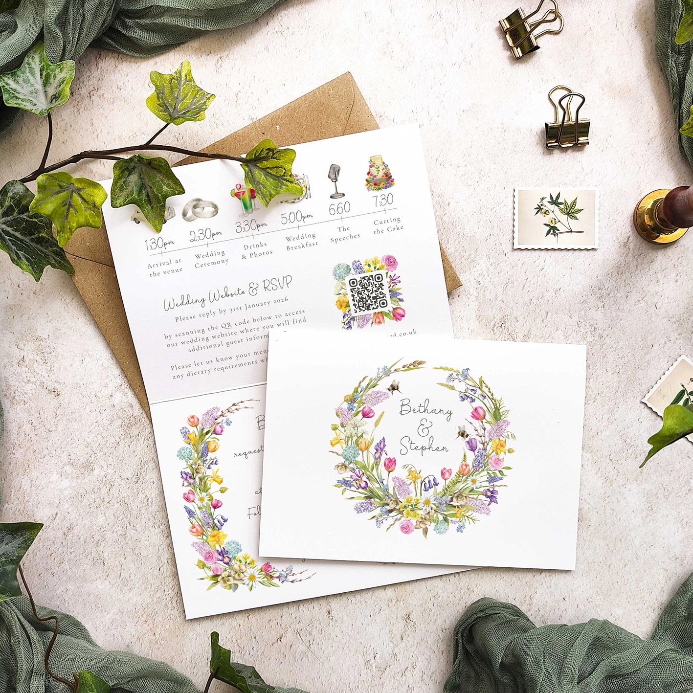 Wedding invitation set with floral design on a textured surface with greenery.