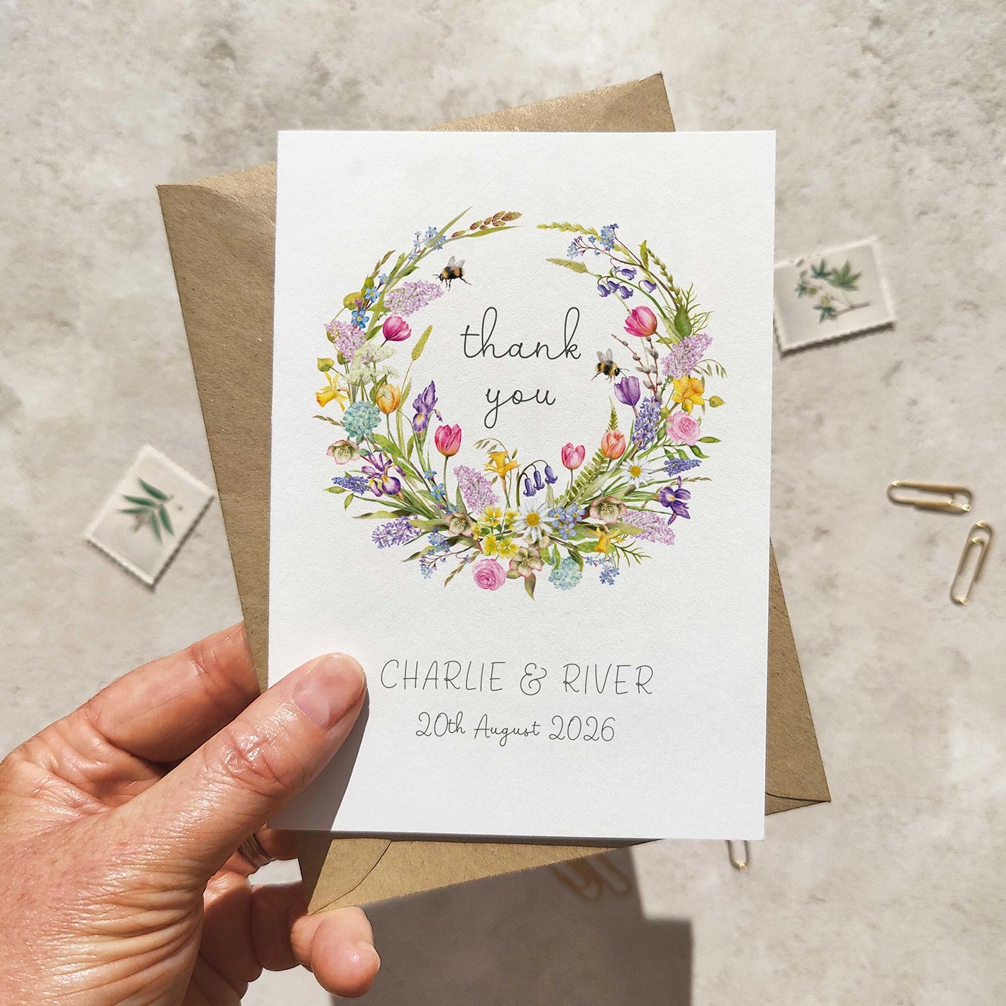 Hand holding a card with a floral wreath design and text on a textured surface.