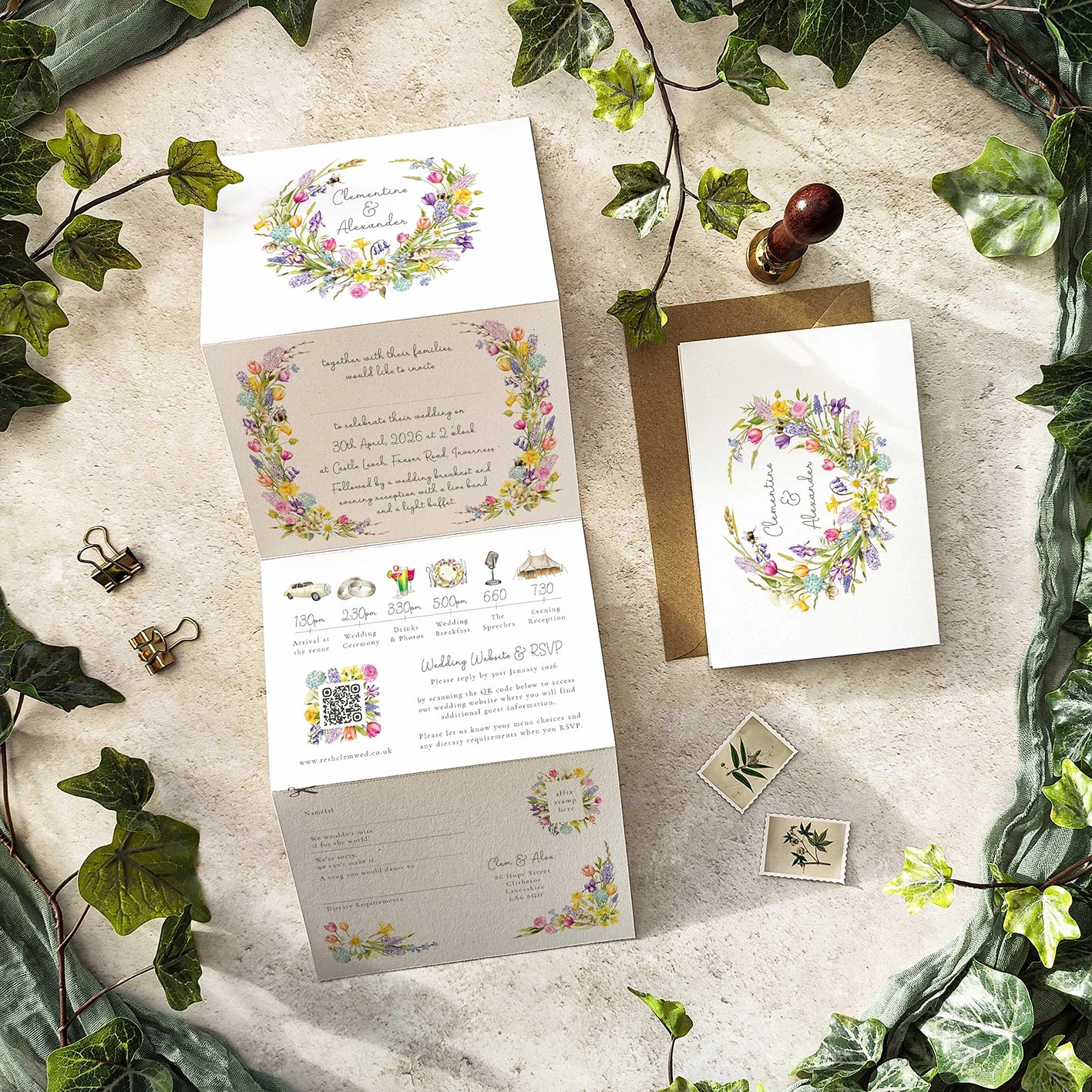 Wedding invitation set with floral designs on a stone surface with greenery.