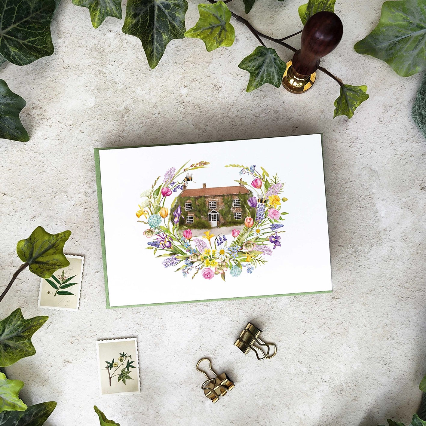 Wedding Invitation Card with floral wreath and house design on a textured surface with ivy leaves.