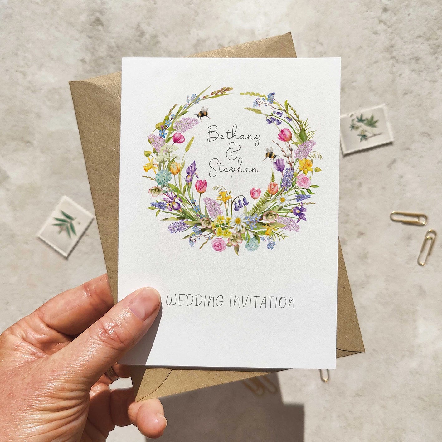 Hand holding a wedding invitation card with floral design and 'Wedding Invitation' text.