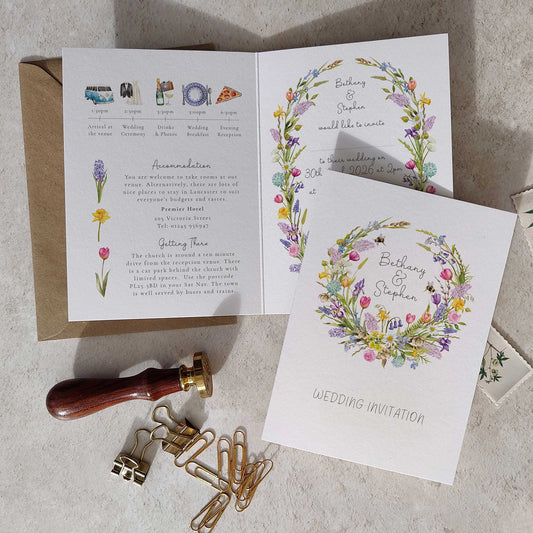 Wedding invitation card with floral design on a textured surface with stationery items.