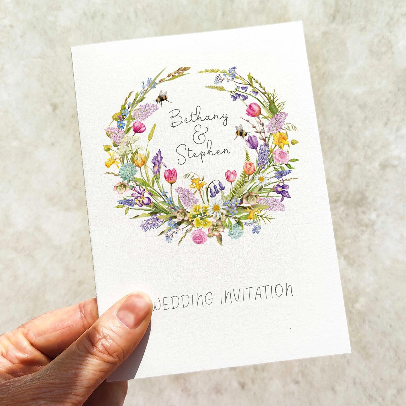 Hand holding a wedding invitation card with floral design and text on a light background