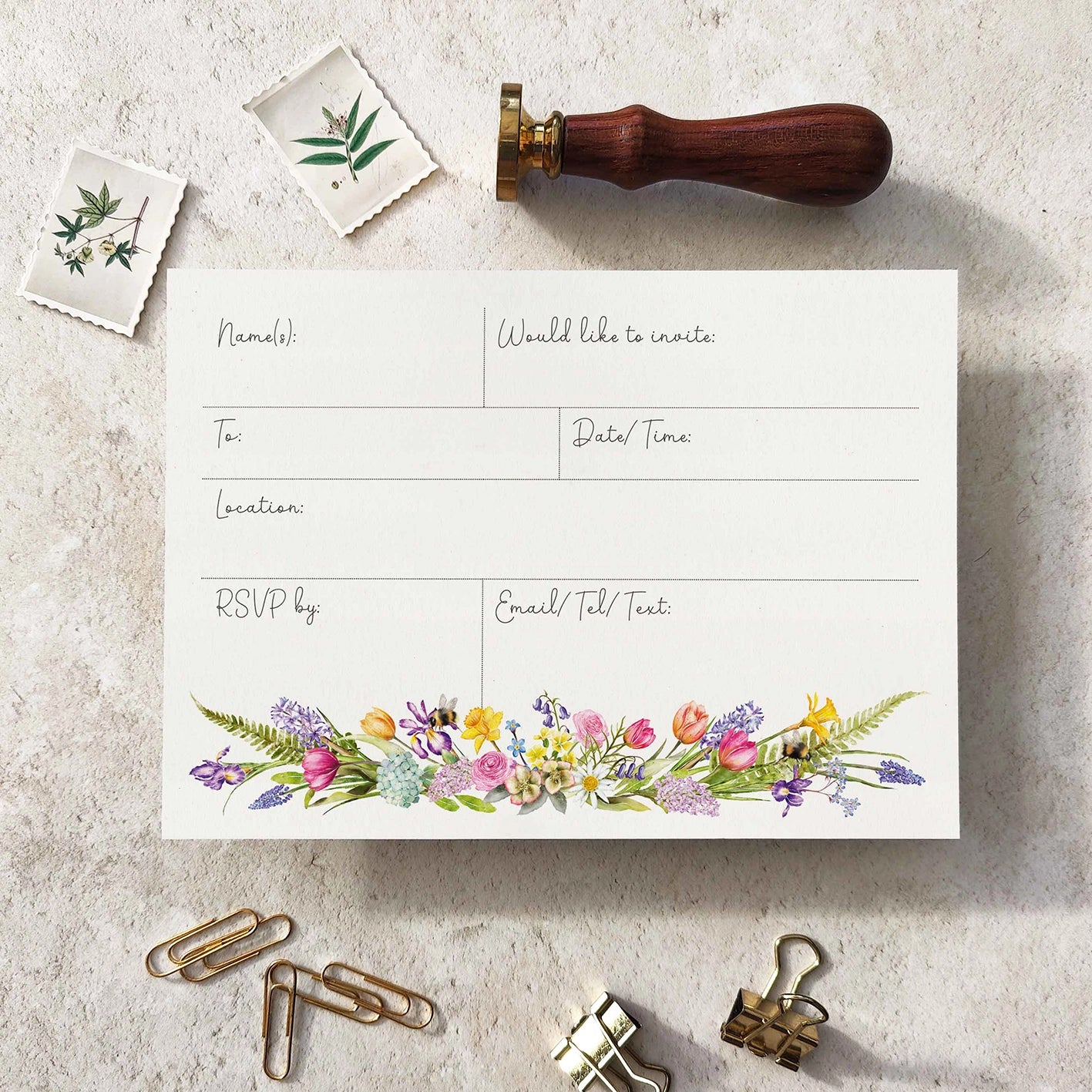 Invitation card with floral design, stamp, and paper clips on a textured surface