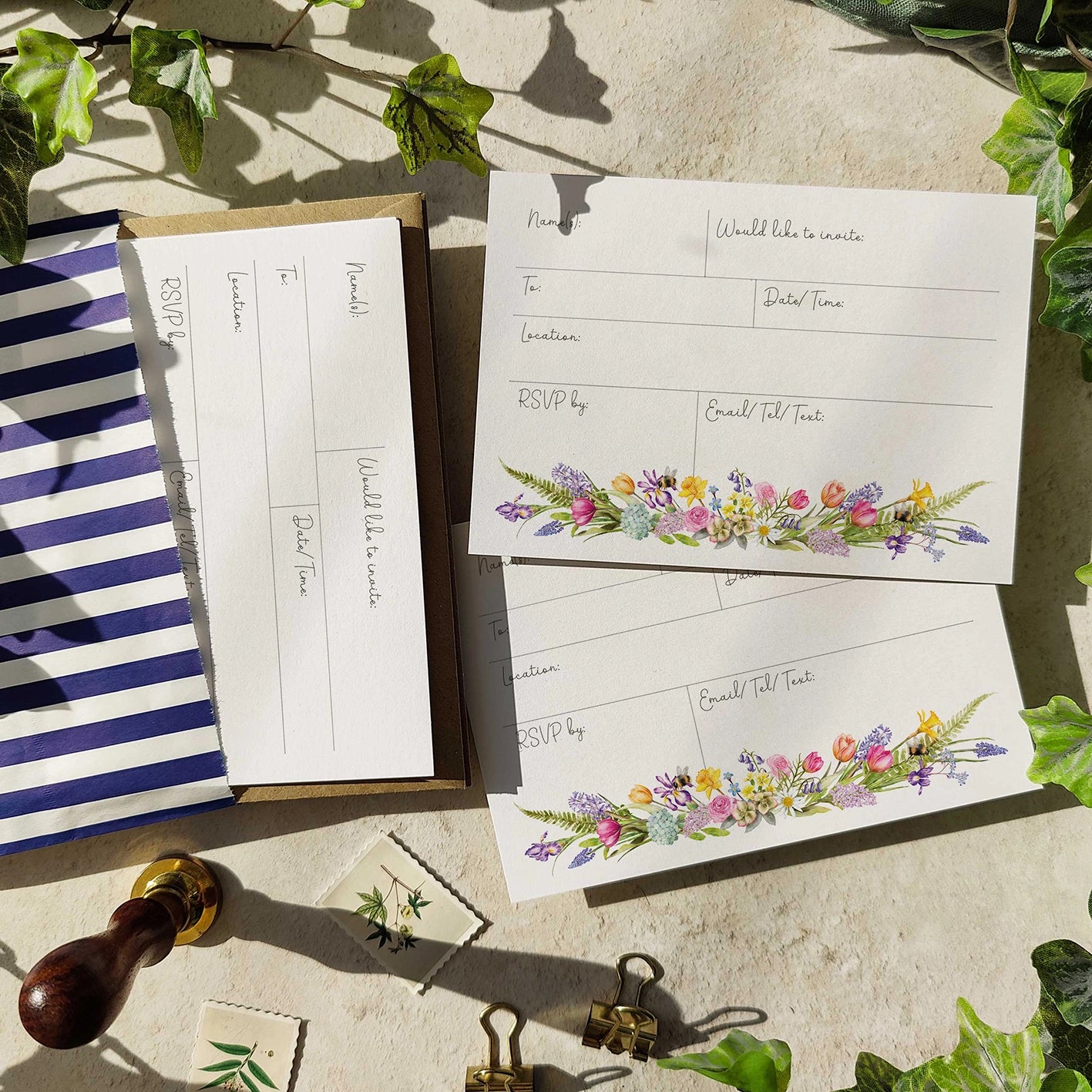 Floral invitation cards with RSVP space on a stone surface with greenery.
