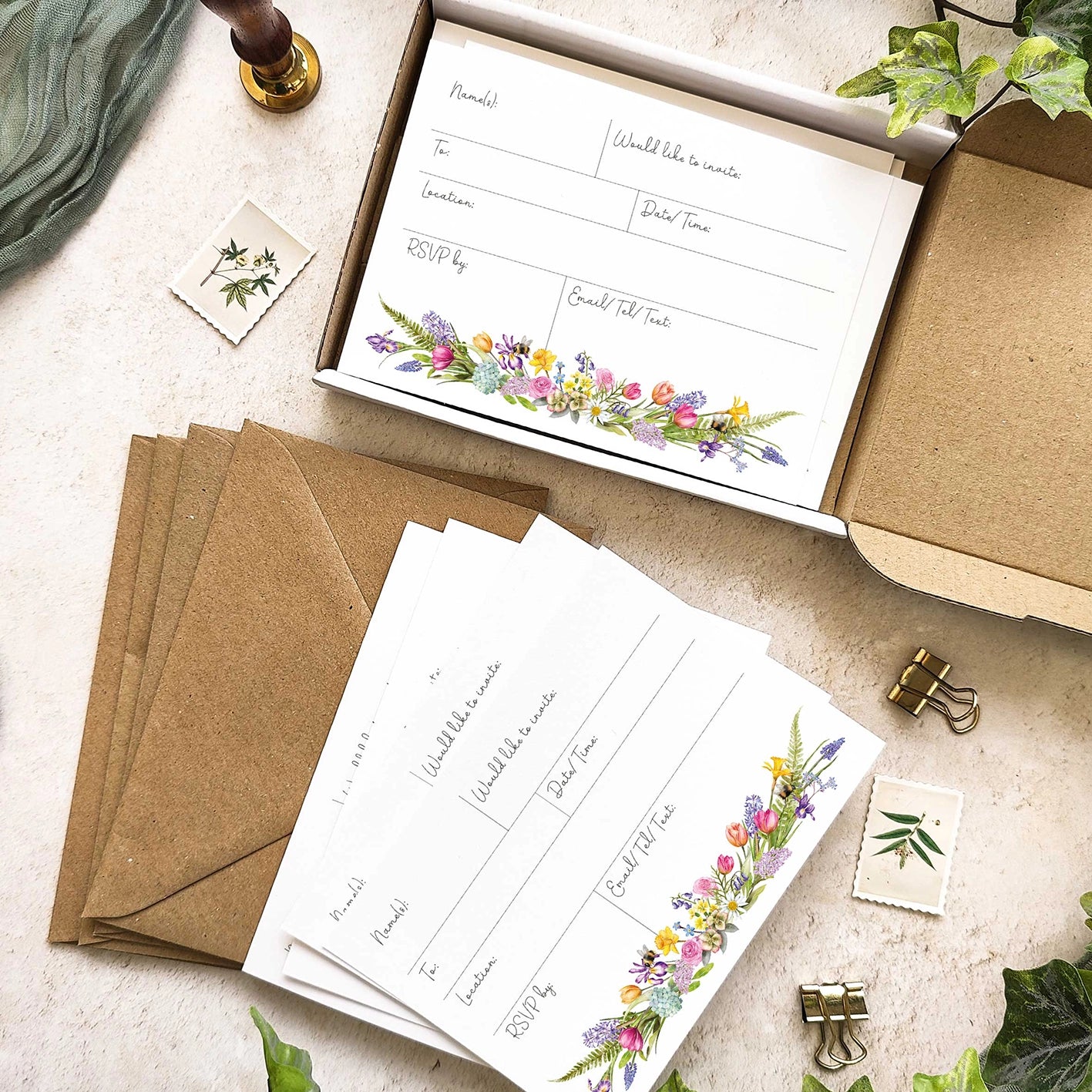 Invitation cards with floral designs on a beige surface with envelopes and stationery items.