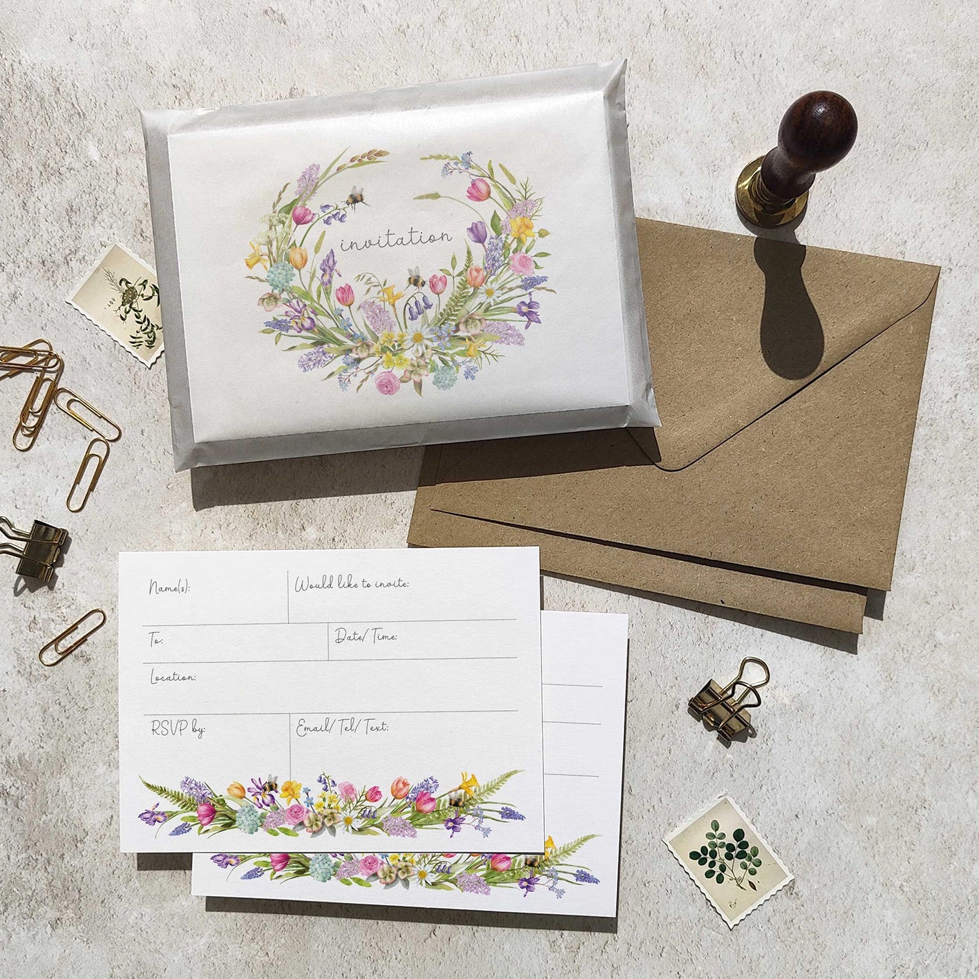 Invitation card with floral design, envelope, and stationery items on a textured surface