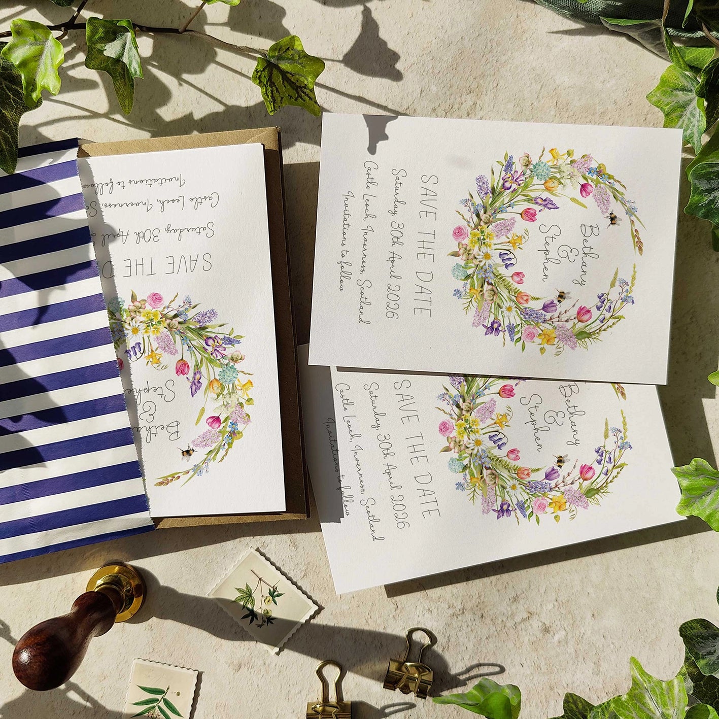 Wedding invitation cards with floral designs on a stone surface with greenery.