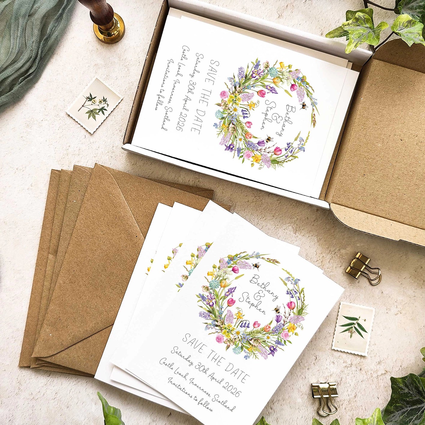 Wedding save the date cards with floral wreath design on a textured surface.