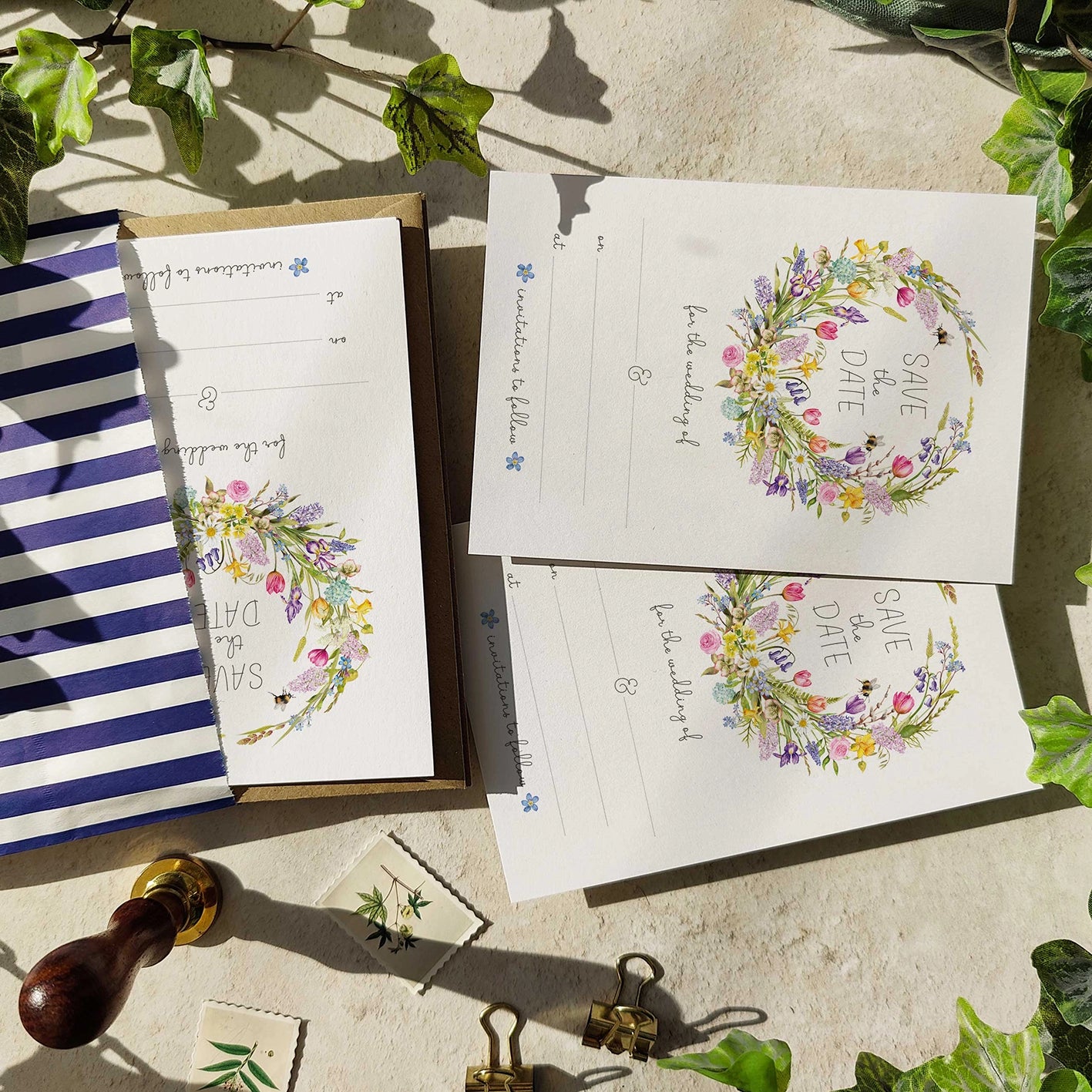 Save the date cards with floral wreath design on a stone surface with greenery.