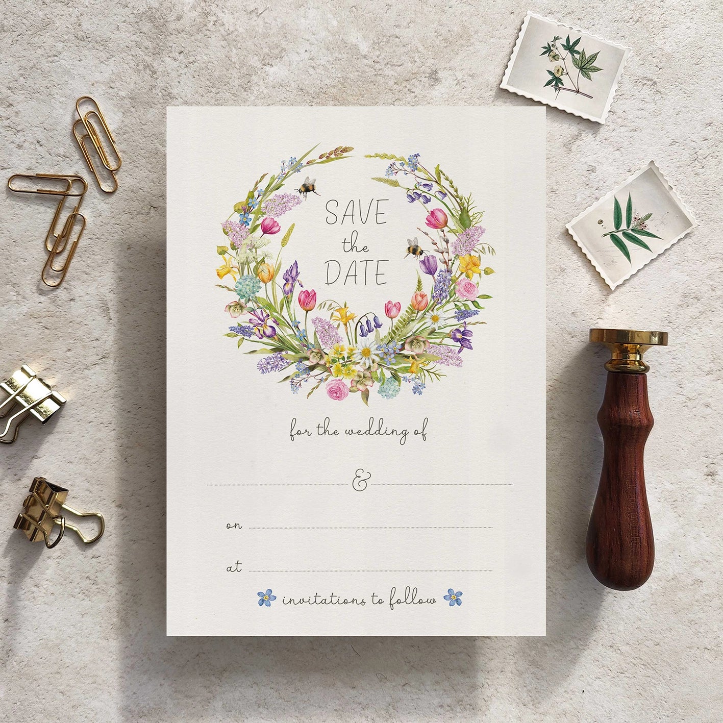 Save the date card with floral wreath design on a textured surface with stationery items.