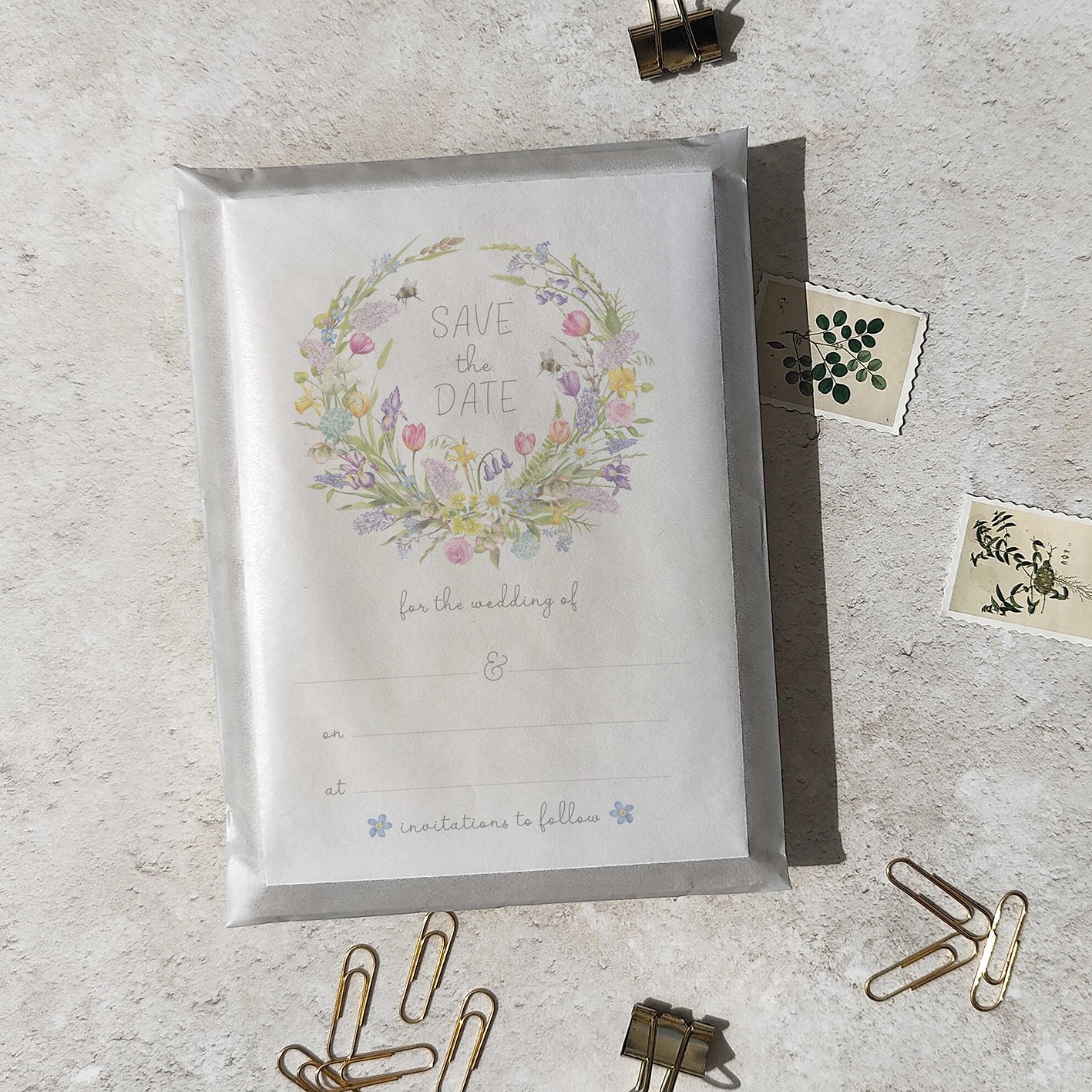 Save the date card with spring floral wreath and 'Save the Date' text on a textured surface with decorative items.