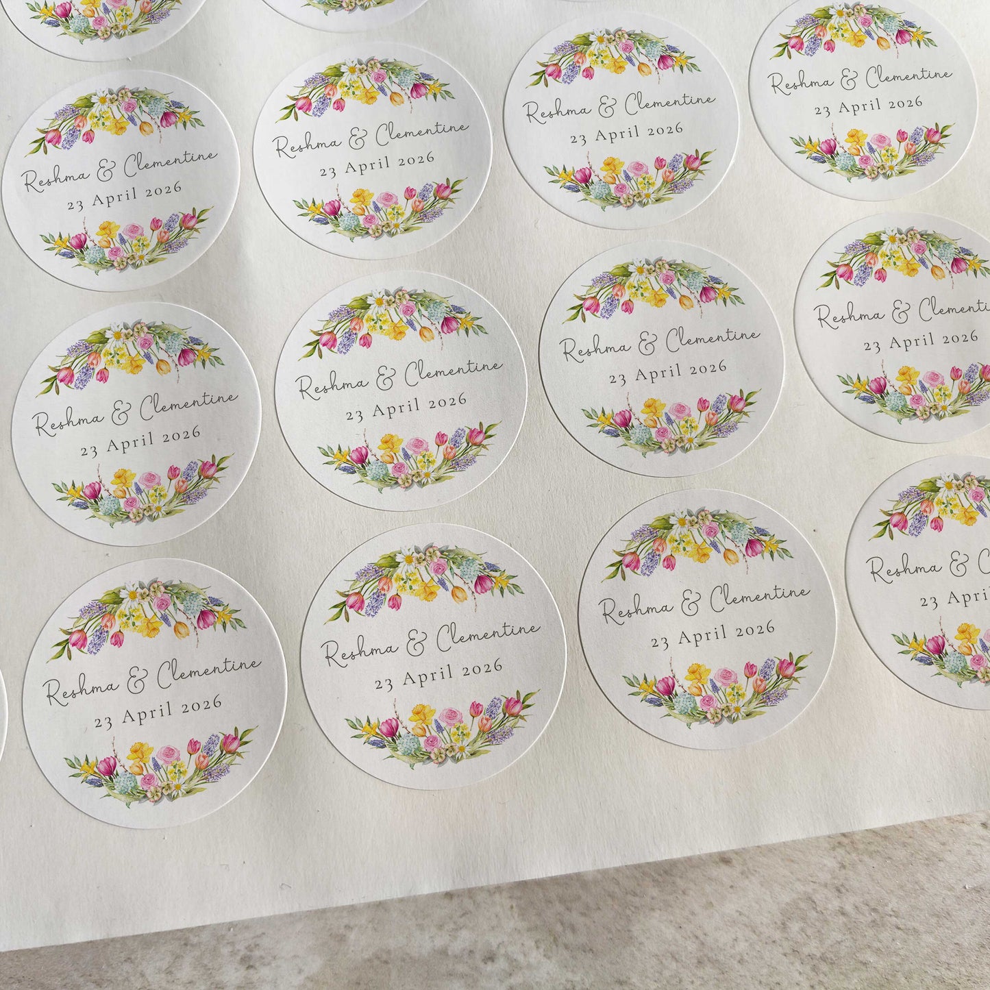 Sheet of round wedding stickers with floral designs and text on a gray surface.