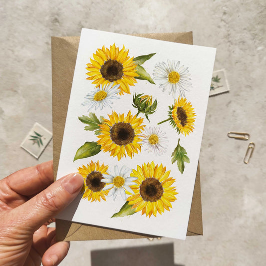 Hand holding a card with sunflower and daisy design on a textured surface