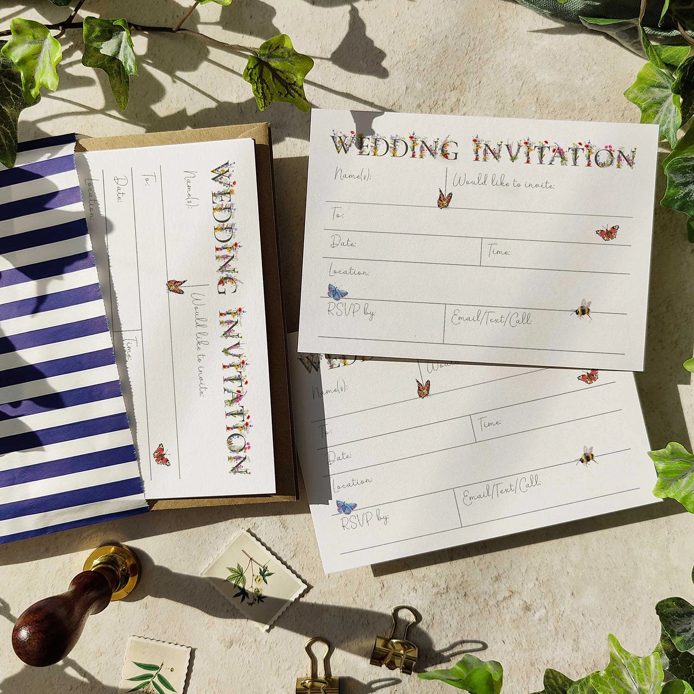 Wedding invitation cards with decorative elements on a stone surface with greenery.