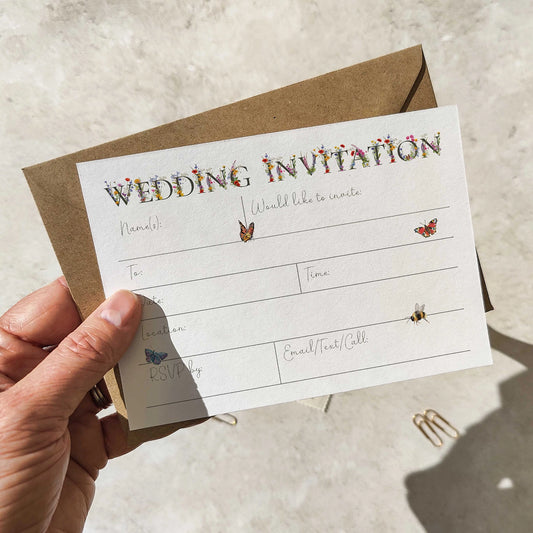 Hand holding a wedding invitation card with decorative elements on a neutral background
