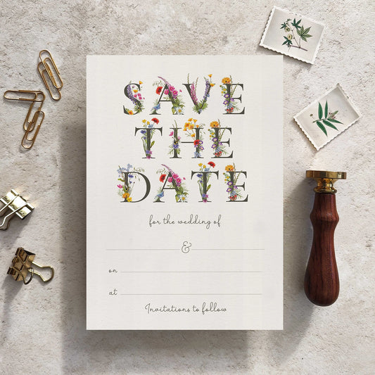 Save the date card with floral text on a textured surface with stationery items.