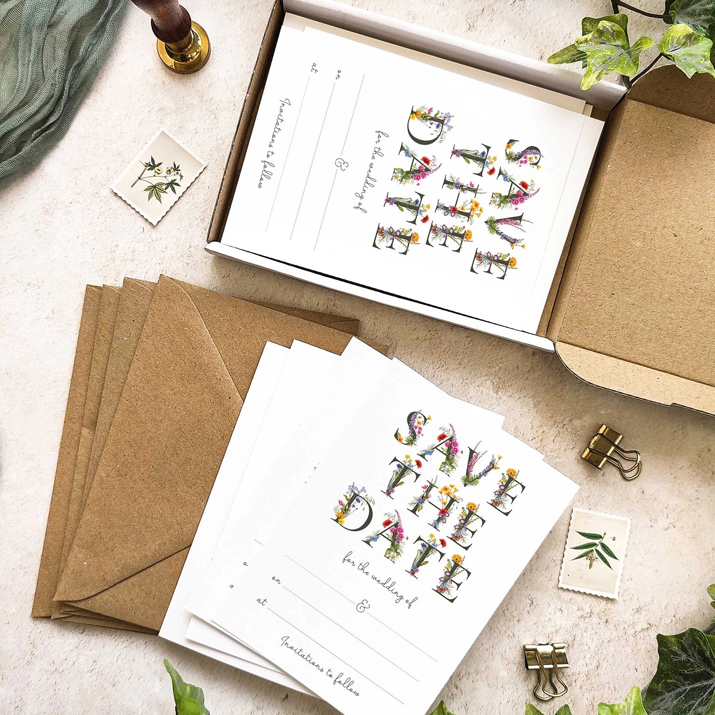 Wedding save the date cards with envelopes and decorative elements on a textured surface.