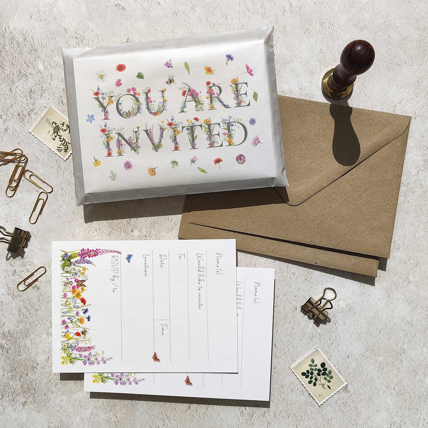 Invitation card with floral text, envelope, and stationery items on a textured surface