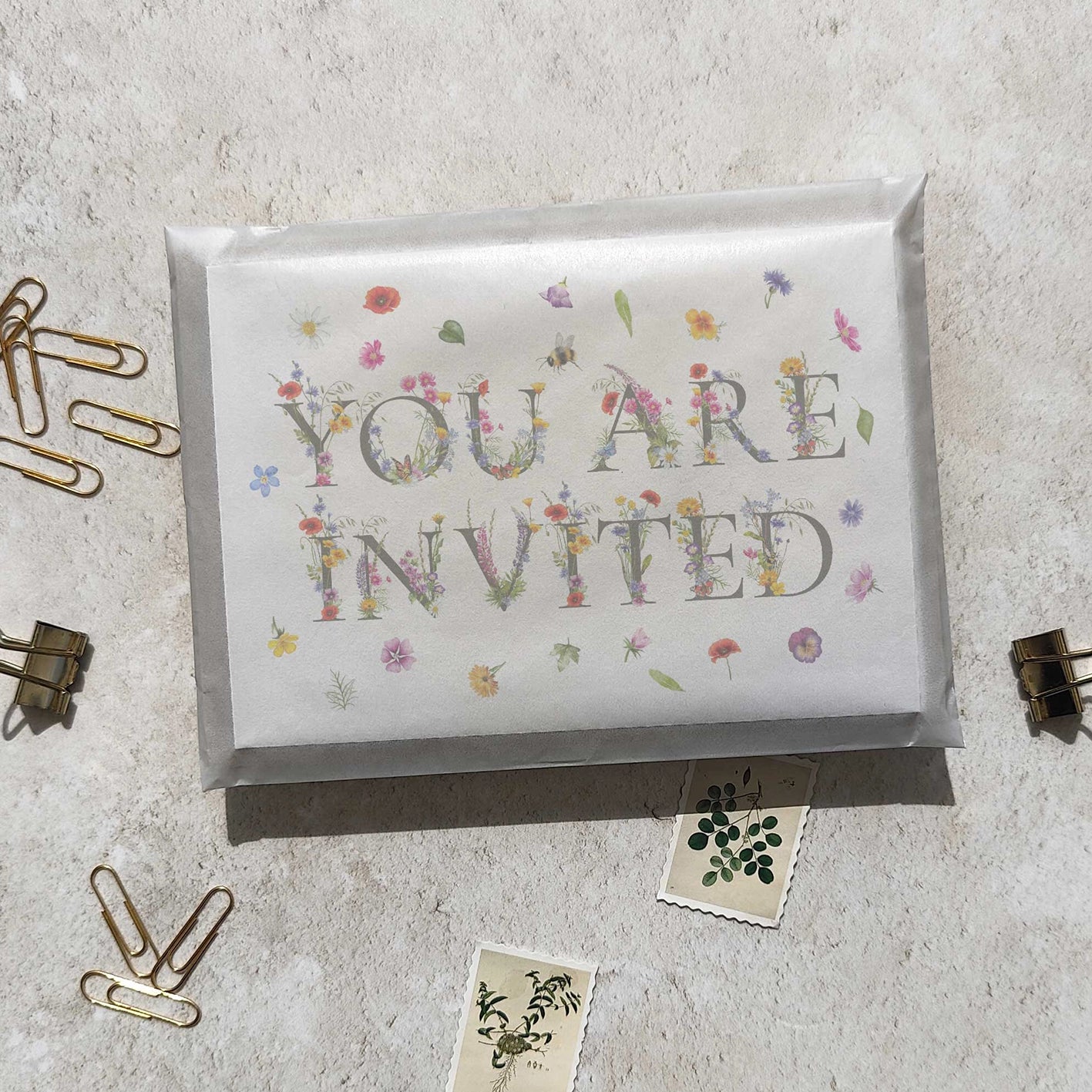 Invitation card with 'You Are Invited' text on a textured surface with paper clips and a small card.