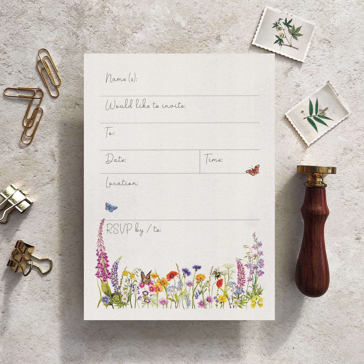 Invitation card with floral design on a textured surface with stationery items.
