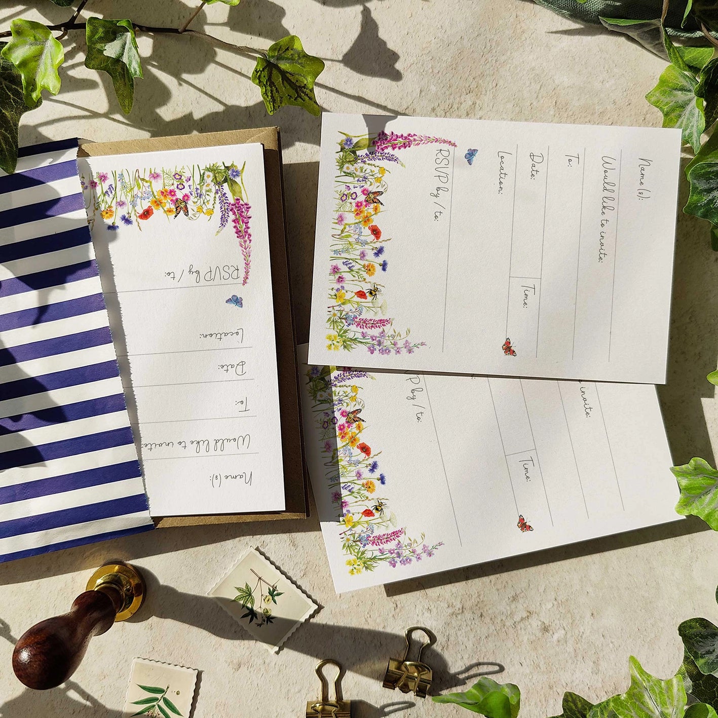 Floral-themed notepads with a striped bag on a stone surface with greenery.
