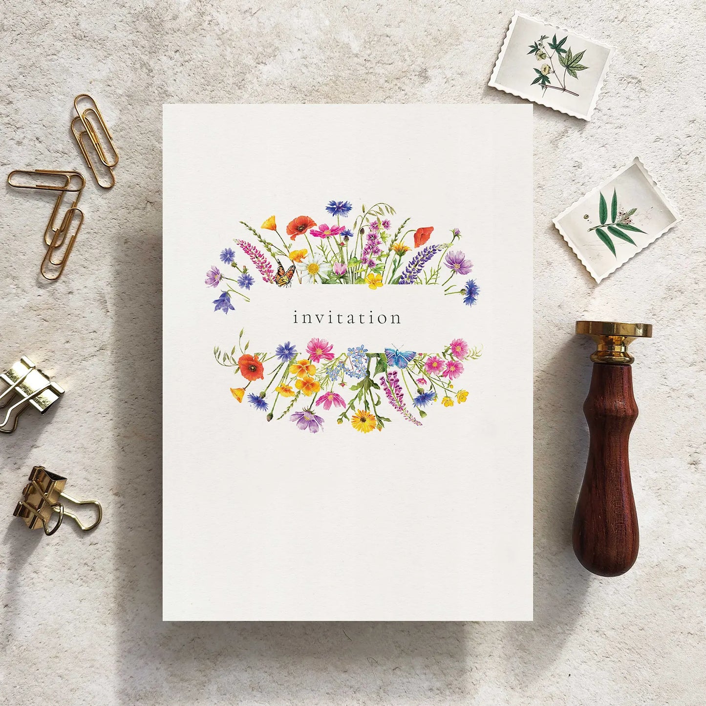 Floral invitation card on a textured surface with stationery items.